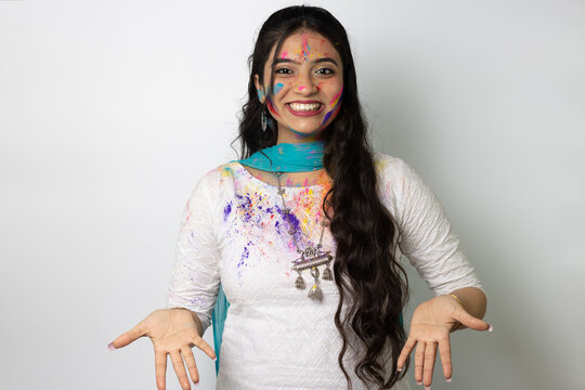 Young indian girl with powder colours on her face for festival of colours Holi, a popular hindu festival celebrated across india, isolated over white background, selective focus advertisement pose