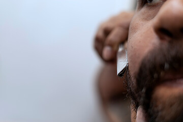 Latin man (39) in front of the mirror uses a razor to shave his beard. Close-up. Barber shop...