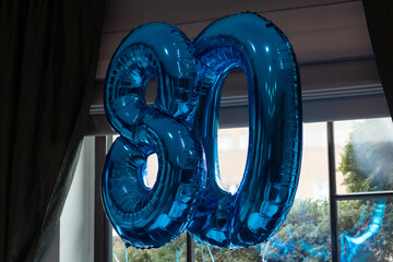 80th birthday balloons are mounted by a window in a restaurant before a birthday party.
