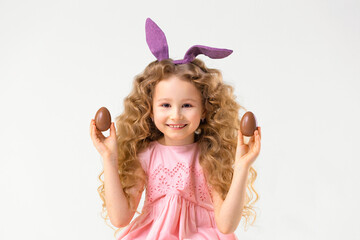 Happy holiday easter kids. Smiling cute little beautiful girl with rabbit hare bunny ears playing with chocolate eggs