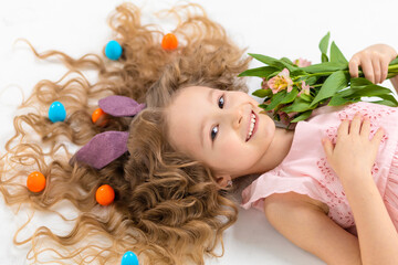 Happy holiday easter kids. creative little beautiful smiling girl with rabbit hare bunny ears, colorful eggs in hair, spring flowers