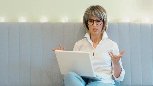 An angry businesswoman indignantly communicates with her subordinate employees on the phone and solves business issues online on the phone and laptop, sitting at home.