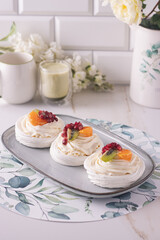 Obraz na płótnie Canvas dessert pavlova with cream and fruits on gray plate white scandic ground white spring flowers matcha tea