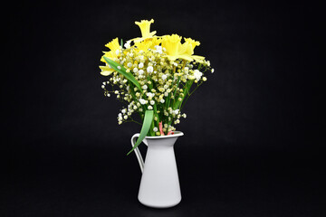 Yellow daffodils with white flowers of the Gypsophila 
in the white tinny vase on a black background. 
Focus is on the center of the image. 