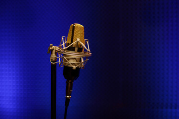 Professional microphone in a recording audio studio with acoustic panels behind it, and blue light on a background.