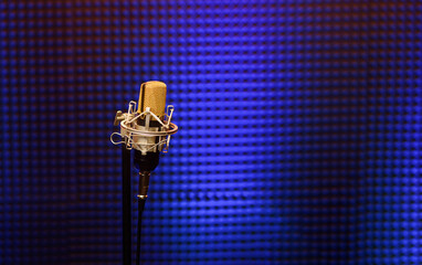 Professional microphone in a recording audio studio with acoustic panels behind it, and blue light...