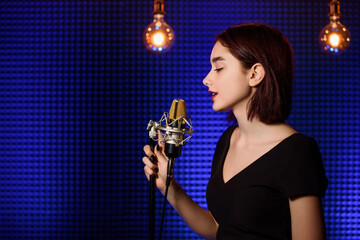 Young woman singer  is recording a song in an audio recording studio.