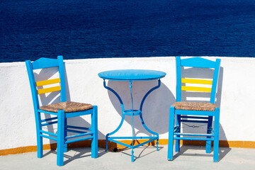 Blue chairs and table on a terrace in the sunshine, overlooking the blue sea in Santorini, Greece