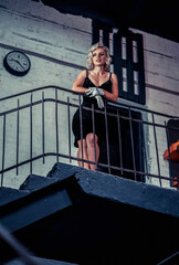 Fototapeta na wymiar blonde in a black dress and white gloves stands on the stairs