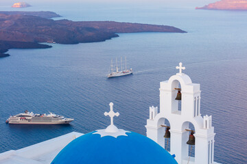 Fototapeta na wymiar White church with blue dome roof overlooking cruise ships on Aegean sea, Santorini, Greece.
