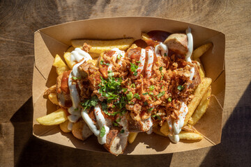 Top view, Currywurst, grilled pork sausage on top with curry powder served with curry ketchup sauce, Mayonnaise and Fried potatoes on paper plate and wooden outdoor table. 