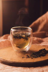 A glass cup of fragrant green tea on a wooden board next to scattered dry tea. steam over a hot drink. Brew tea.