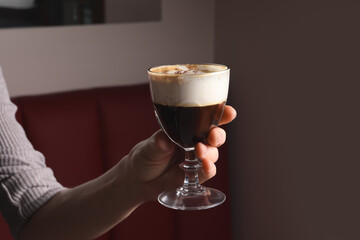 Woman holding glass of aromatic coffee drink with chocolate powder in cafe, closeup