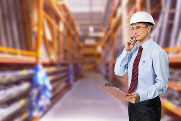 An inspector with a helmet on his head, stands in the warehouse and checks inventory on the tablet.