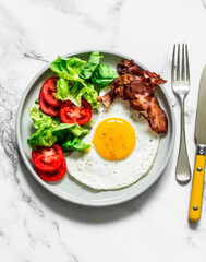 Breakfast plate - fried egg, bacon and vegetables salad on a light marble background, top view