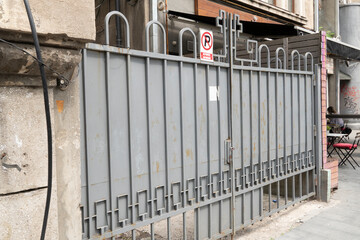 Delicate, smart metal gate with strong line details that keeps privacy while provide security for a private property in an alley with no parking sign to keep away cars that may obstruct the gate.