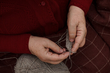 Top view close-up plump wrinkled hands of an elderly woman in a burgundy sweater with a plaid...
