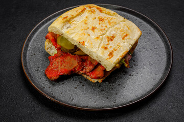 sandwich with smoked meat, pickled cucumbers and herbs. on a plate on a dark background