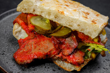 sandwich with smoked meat, pickled cucumbers and herbs. on a plate on a dark background