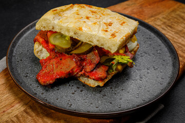 sandwich with smoked meat, pickled cucumbers and herbs. on a plate on a dark background