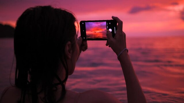 Young Attractive Tourist Girl Taking Photos of Amazing Colourful Sunset Sky. Female in Bikini Making Photos with Smartphone near Beach. High Quality 4K Slowmotion Tropical Life. Phuket, Thailand.