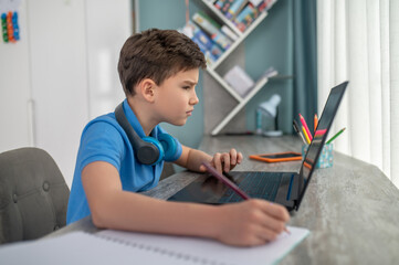Schoolboy seated at the desk staring at his laptop screen