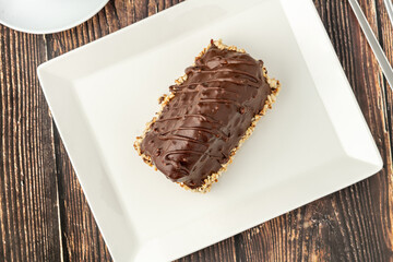 Dessert Cake from Malaga on wooden table. Cake with banana inside, covered with chocolate sauce and hazelnuts.