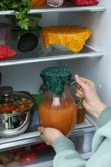 Woman taking jug covered with beeswax food wrap from refrigerator, closeup