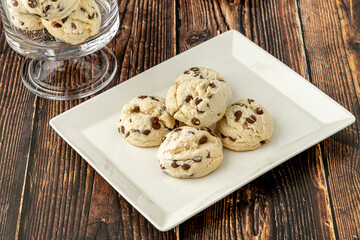 Stacked chocolate chip cookies in white plate on wooden table