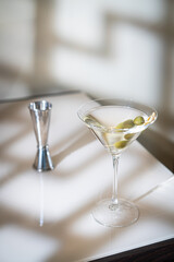 Cocktail vodka martini with green olives on light background with bright beautiful shadows