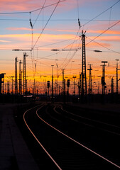 Fototapeta na wymiar Sunset panorama with colorufl sky and warm atmosphere at Dortmund main station Germany. Railway tracks, signals, catenary and high voltage overhead lines with reflections of sunlight. Public transport