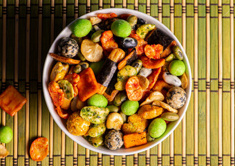 Various Japanese snacks in a wooden bowl close-up. Rice crackers with wasabi and nori, peanuts with sesame seeds, and other snacks. Mix traditional Japanese snack food.