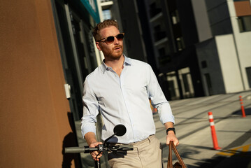 Fototapeta na wymiar Young stylish businessman with e-scooter. Portrait of handsome man outdoors