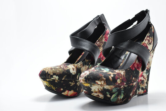 Zapatos negros de plataforma con diseño de flores de colores. Zapatos de mujer sobre un fondo blanco con espacio para texto al lado izquierdo.