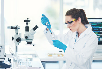 Shes in concentration mode. Cropped shot of a focused young female scientist wearing protective glasses while pouring a test sample into a vile inside of a laboratory.