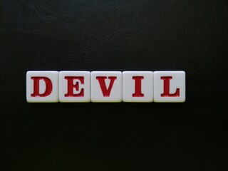 The word Devil is spelled with white and red tiles on a black leather background sheet