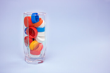 Waste multicolored plastic lids in a water glass