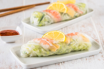 Two summer rolls with salad and prawns on a white wooden background, japanese, asian food