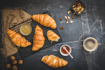 Breakfast scene with croissants, honey, jam and coffee and nuts, black background, top view