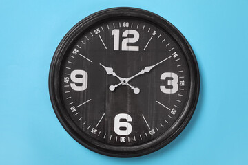 Stylish analog clock hanging on light blue wall