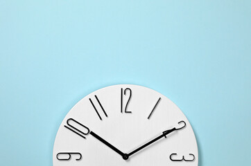 Stylish analog clock hanging on light blue wall, space for text