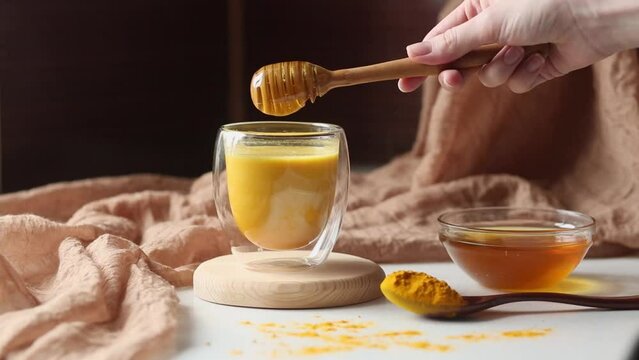 Turmeric latte, preparing golden milk in the kitchen. Honey drips from a spoon. Hot healthy drink. Milk, turmeric, honey