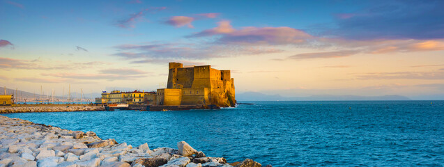 Naples, Italy. Castel dell'Ovo with breakwater rocks in the foreground and with a beautiful sunset...