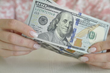 Women's hands hold dollars in cash. 1000 dollars in 100 banknotes close-up.