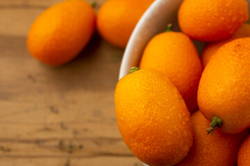 Macro aerial view of wet kumquats, in white bowl, selective focus, on wooden table, horizontal, with copy space