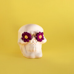 Human skull model, purple spring flowers. Creative arrangement against pastel yellow background....
