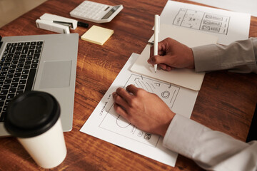 Hands of UI designer drawing wireframes for pages of website or mobile application at his office...