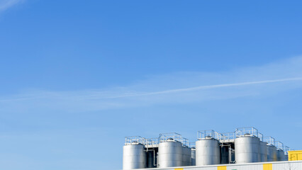 Part of steel tanks of silvery color on a background of the blue sky. Space for text. Winery or petroleum concepts.