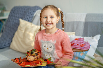 little cute girl is holding a craft made of natural materials. autumn needlework with children. children's cute hedgehog made of natural materials.