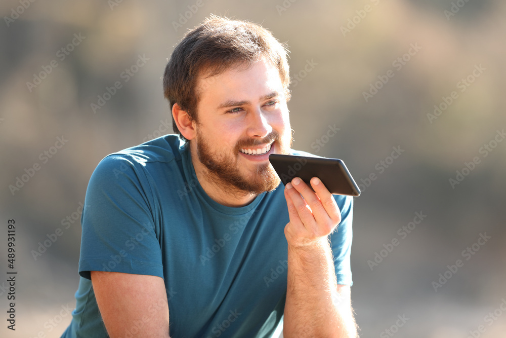 Wall mural happy man using voice recognition on cellphone outdoors